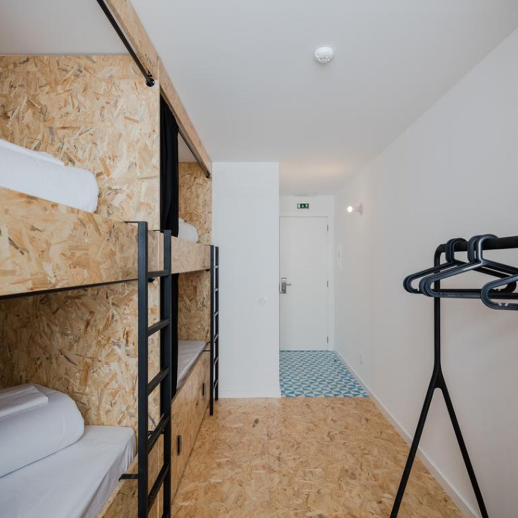 A bunk bed room with a wooden wall, a white door, and a metal drying rack.