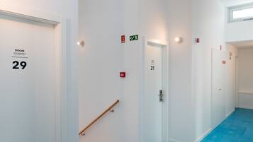 Un couloir avec des portes portant les inscriptions « SALLE QUARTO 29 » et « SALLE QUARTO 21 », un sol recouvert de carreaux bleus et une rambarde.