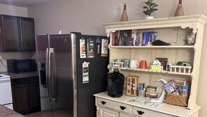 Una cocina con un refrigerador de acero inoxidable, un microondas, un gabinete blanco con manijas negras y una cafetera.