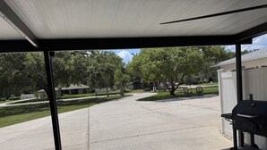 Un patio techado con una parrilla, un camino de hormigón y vistas a un barrio residencial con casas y árboles.