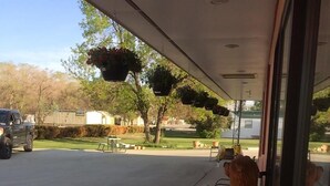 A covered outdoor area with a concrete floor, a bench, and hanging flower baskets. - Wheels Motel (Greybull)