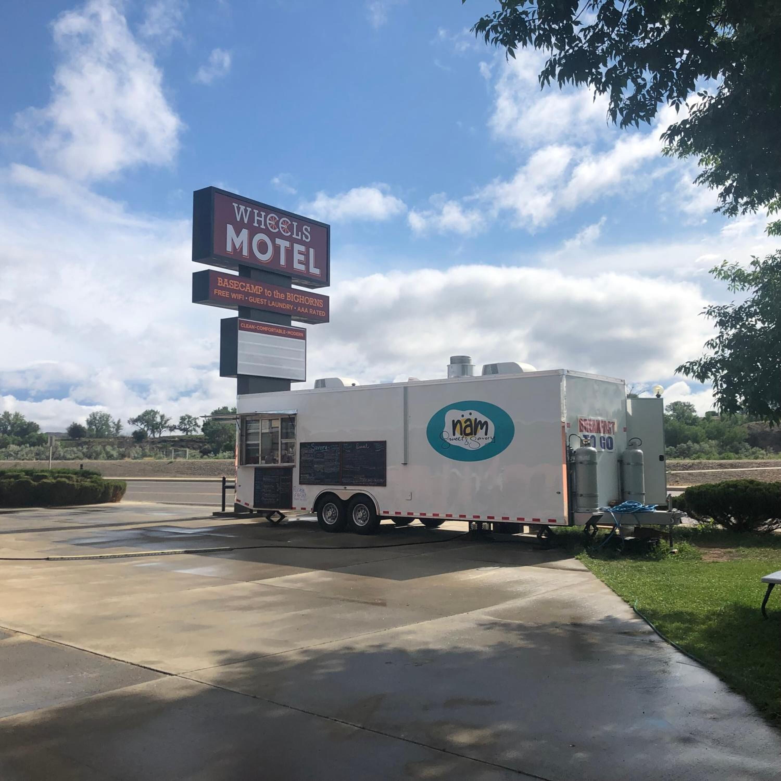Señal del motel Wheels que enumera los servicios, con una camioneta de comida móvil con la marca 'nam' estacionada al frente.