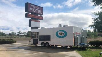 Señal del motel Wheels que enumera los servicios, con una camioneta de comida móvil con la marca 'nam' estacionada al frente.