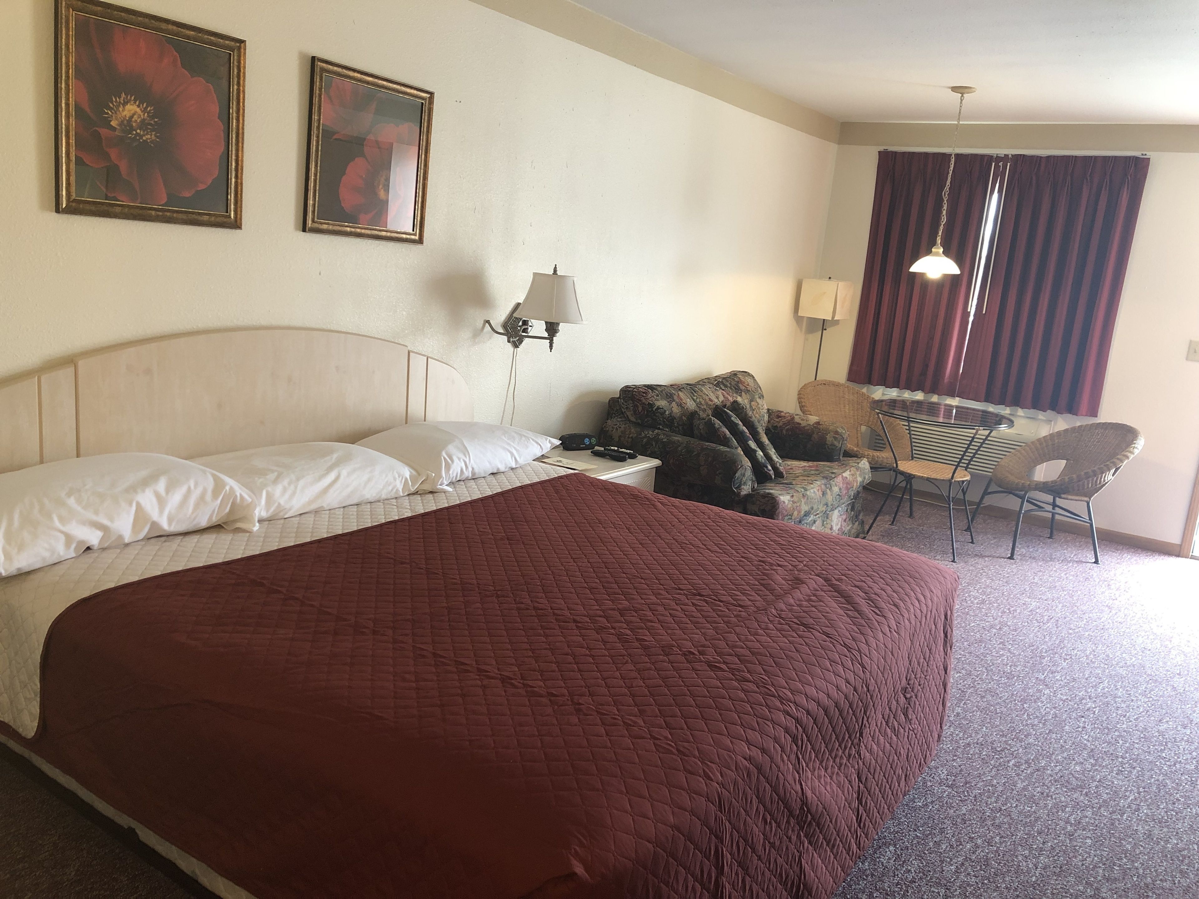 Een hotelkamer met een groot bed, twee wandlampen, een bureau met een stoel en twee ingelijste foto's aan de muur.