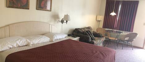 Een hotelkamer met een groot bed, twee wandlampen, een bureau met een stoel en twee ingelijste foto's aan de muur.