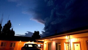 A motel with a car parked in front, a visible moon in the sky, and a cloudy sky. - Wheels Motel (Greybull)