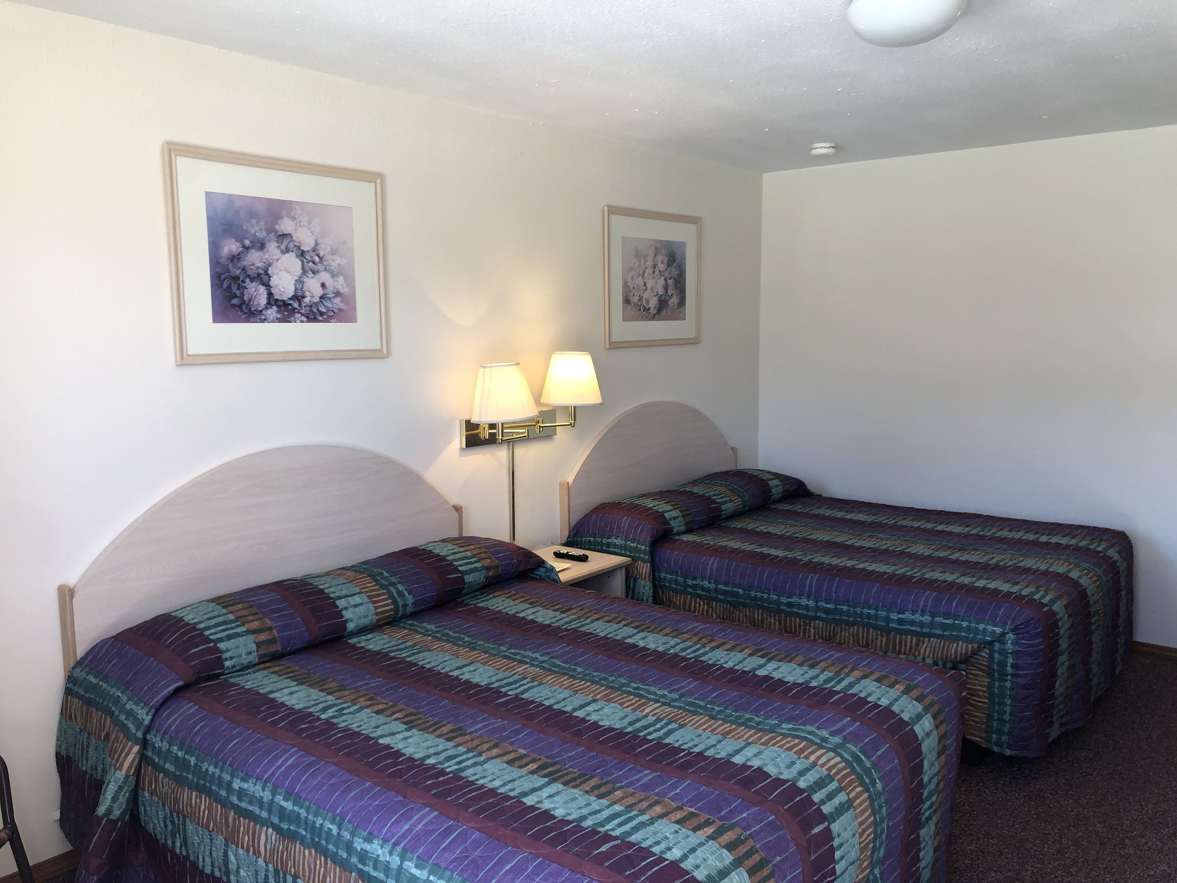 Een hotelkamer met twee bedden, elk voorzien van een gestreept laken, een nachtkastje met een lamp, en bloemrijke kunstwerken in lijsten aan de muren.