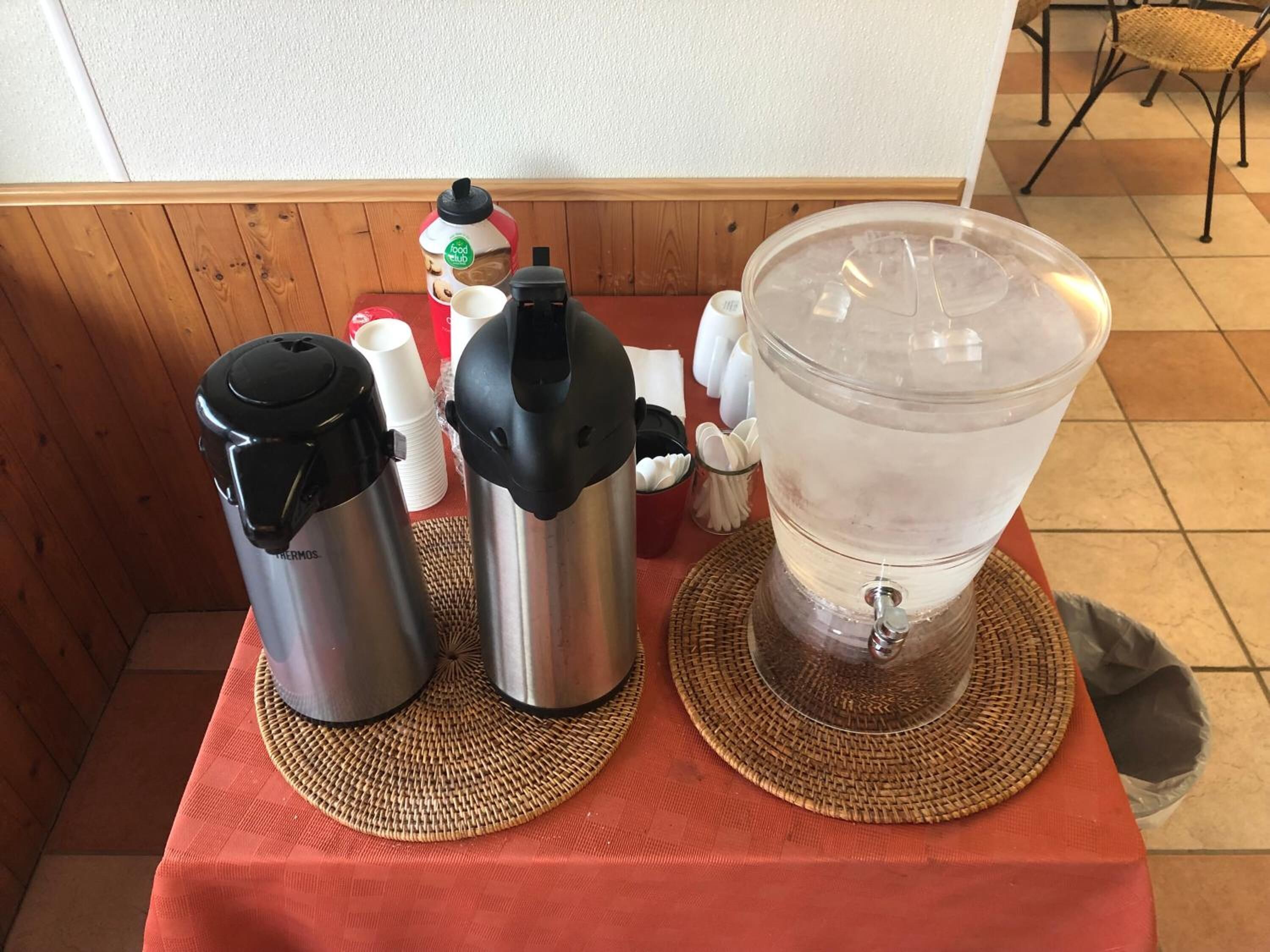 Uma mesa com cafeteira, termo e dispensador de água.