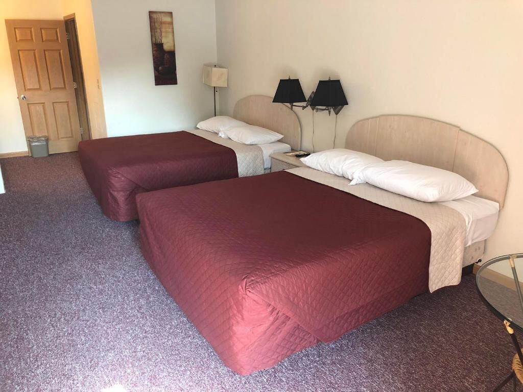 A hotel room with two beds, a small table, and a lamp.