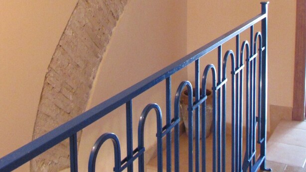 Eine Treppe mit einer gewölbten Steinwand, einem blauen Metallgeländer und einer Wandleuchte.