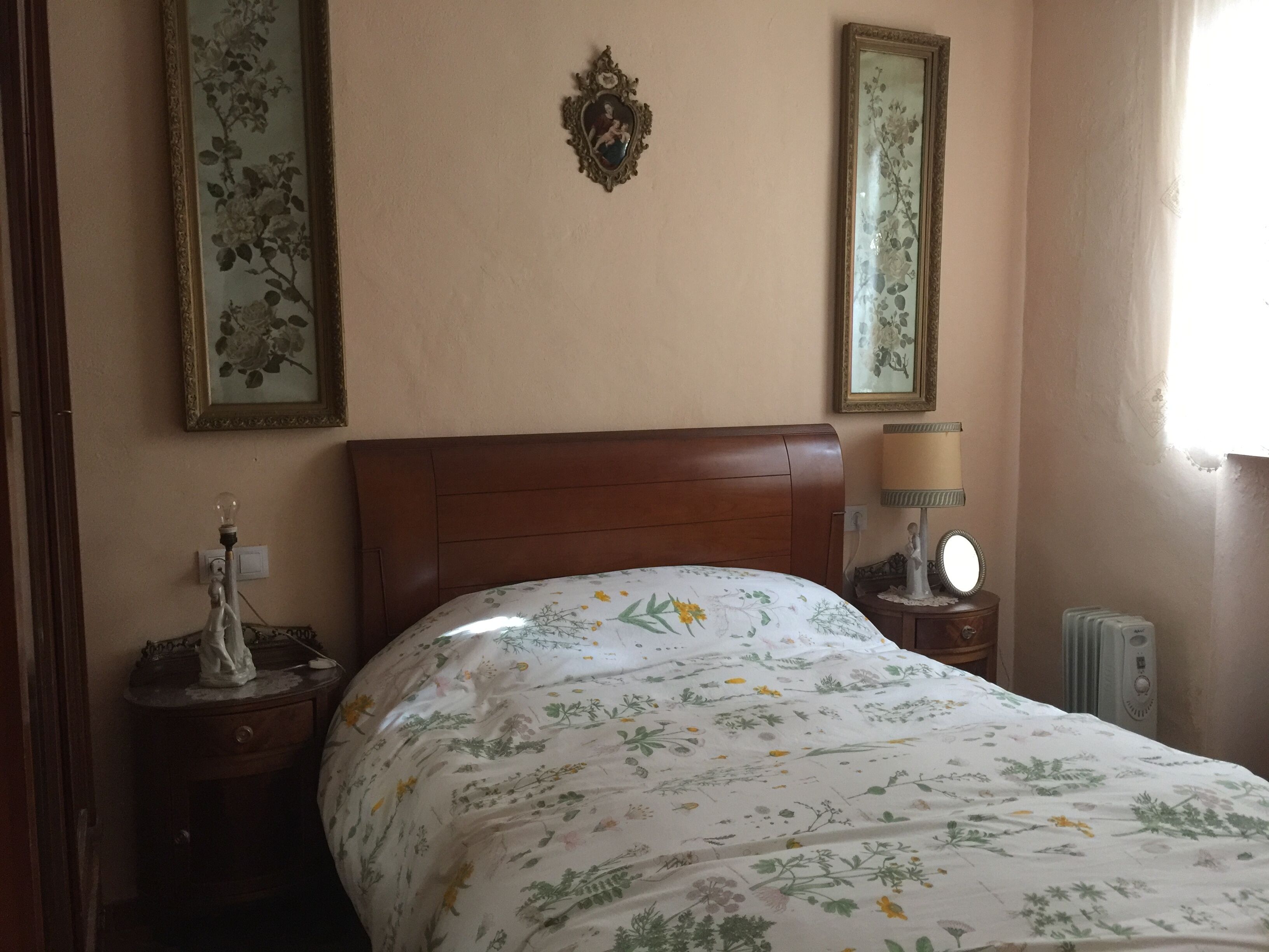 A bedroom with a wooden bed, floral bedding, two wall-mounted mirrors, and a bedside lamp.