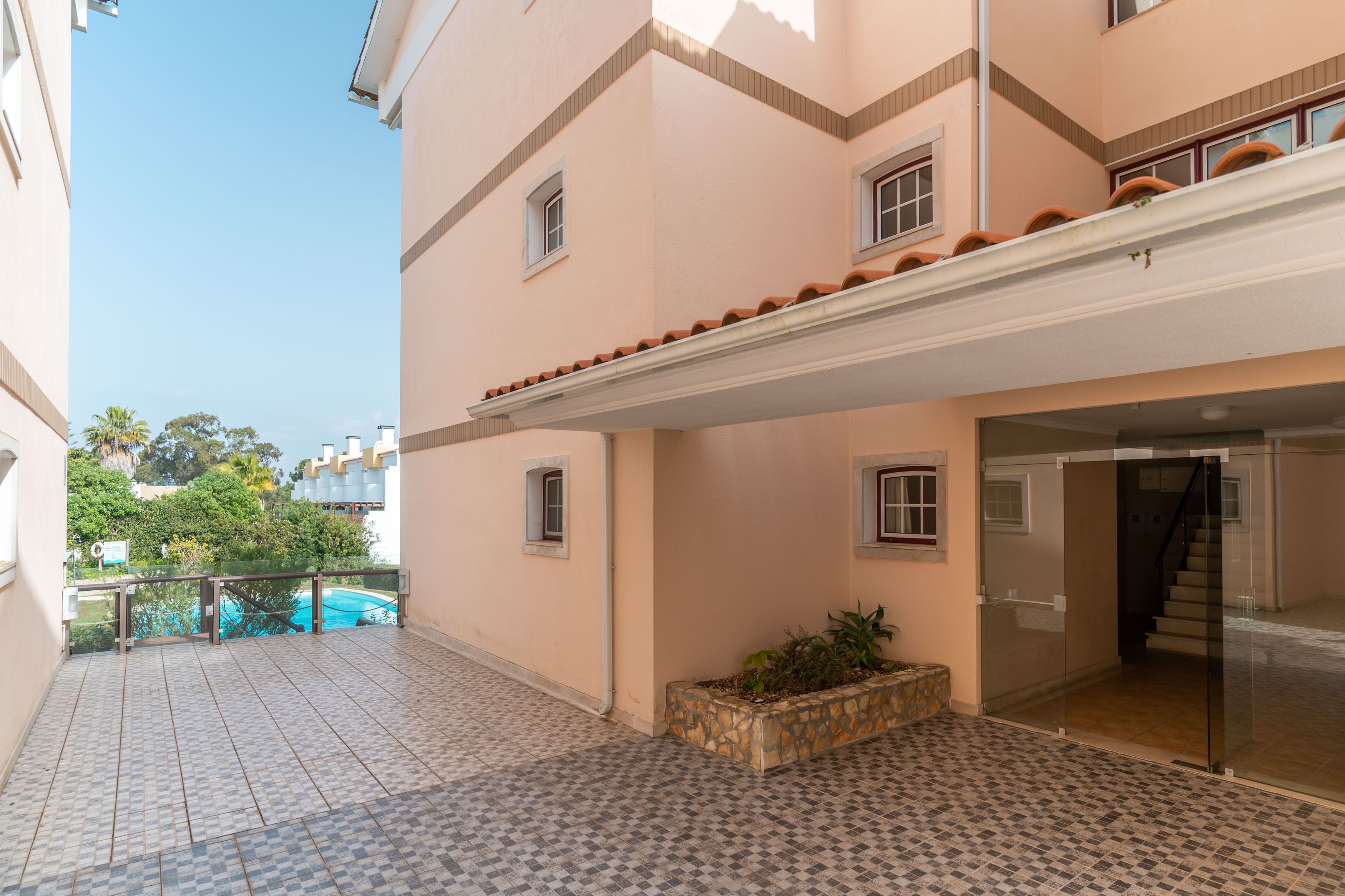 A building with a tiled patio, a small garden, and a pool in the background.