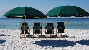 Four beach chairs under green umbrellas with 'WATERS EDGE' branding, positioned on a sandy beach with the ocean in the background.