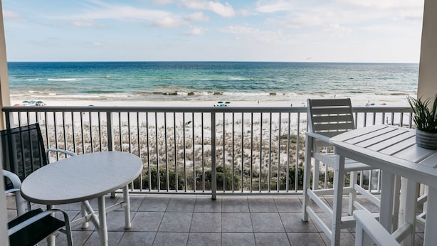 A balcony with a view of the beach, a table, and chairs.