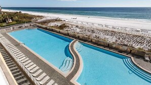 A swimming pool with a curved design, adjacent to a beach and a white sandy area with lounge chairs.