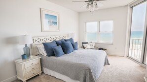 A bedroom with a bed, nightstands, a lamp, a framed picture, and a view of the ocean.