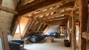 A spacious attic room with a sloped ceiling, wooden beams, a dark blue sofa, a wooden coffee table, and a small wooden chair. - CHARACTER GITE with TERRACE and GARDEN, SPACIOUS and QUIET  (Gueberschwihr)