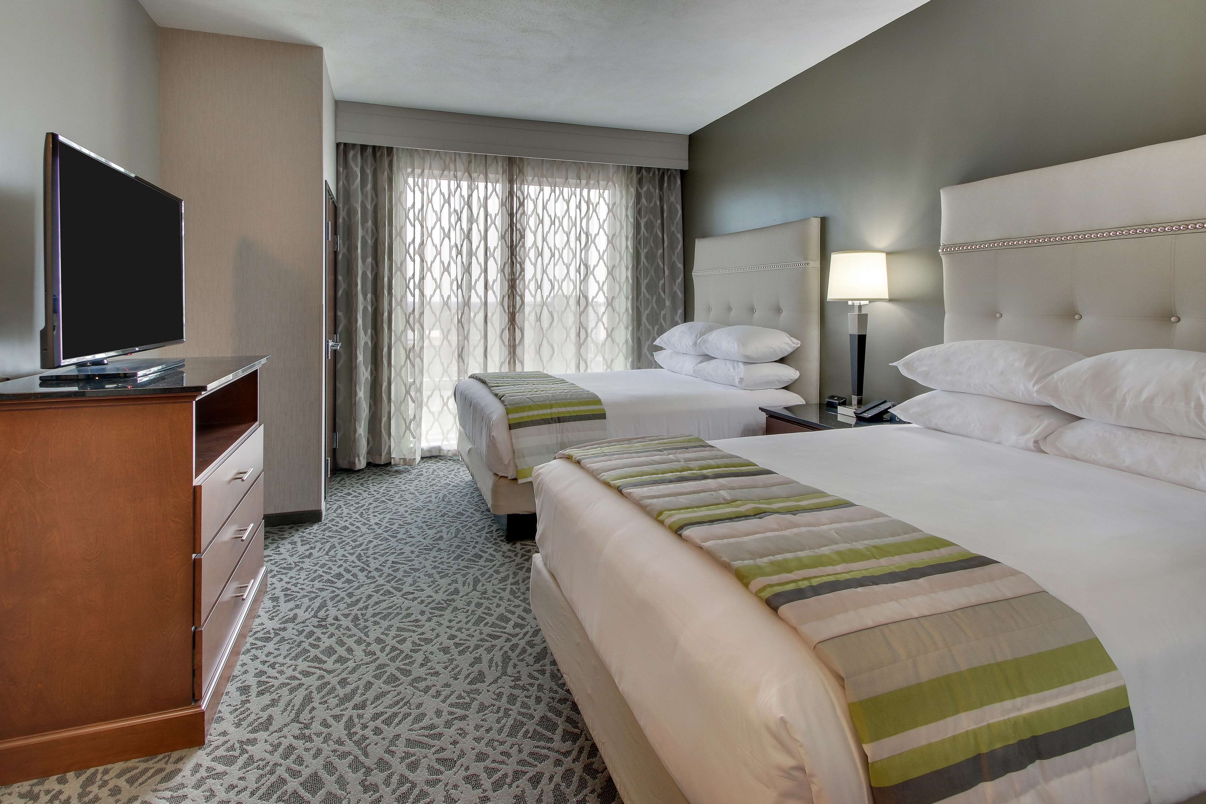 A hotel room with two beds, a TV, a desk, and a lamp.