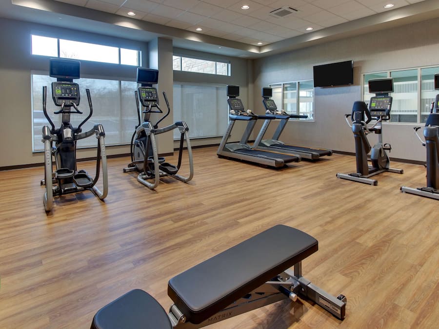 Un gimnasio con cintas de correr, elípticas y un banco.