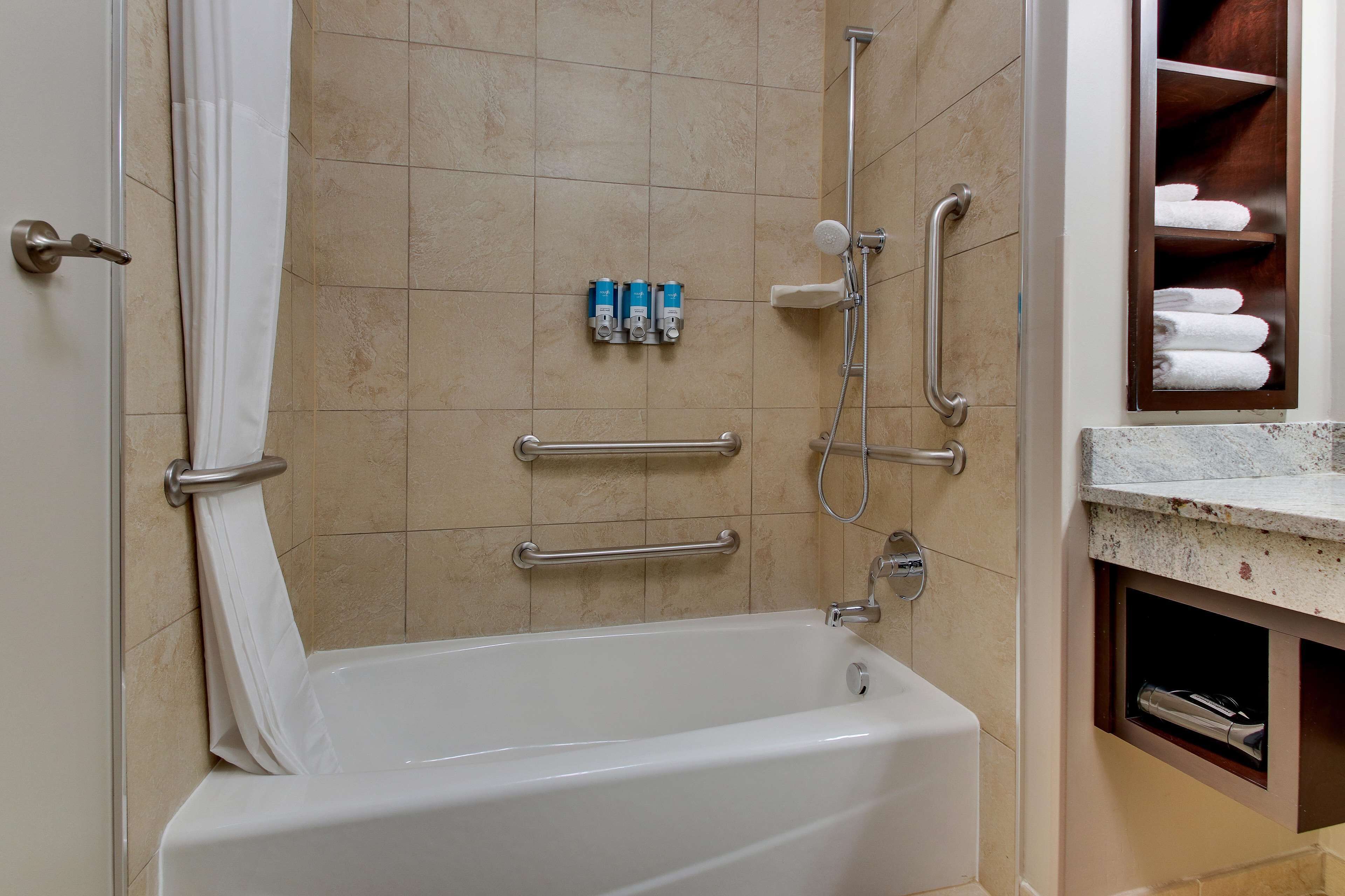Une salle de bain équipée d’une baignoire, de barres d’appui, d’un porte-serviettes et d’une étagère où sont rangées les serviettes.