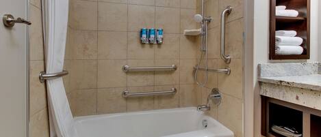 Un baño con bañera, barras de apoyo, toallero y estante con toallas.