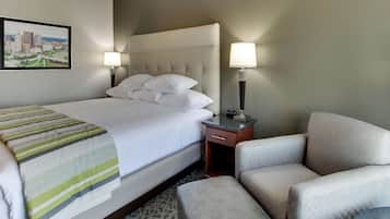A hotel room with a bed, a chair, a nightstand, and a lamp.