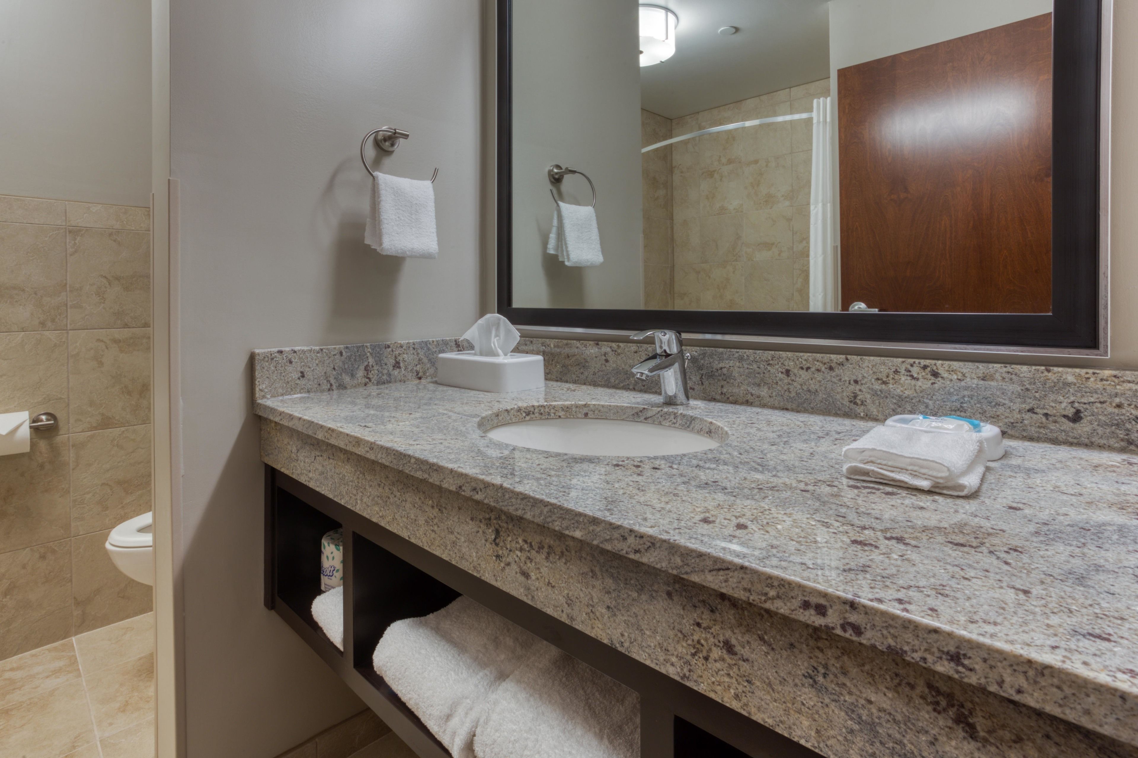 A bathroom with a granite countertop, two sinks, a mirror, and a towel rack.