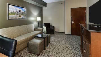 A hotel room with a sofa, a chair, a small table, a TV, and a door.