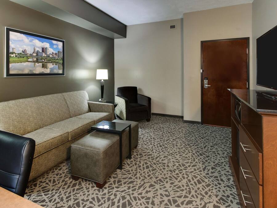 A hotel room with a sofa, a chair, a small table, a TV, and a door.