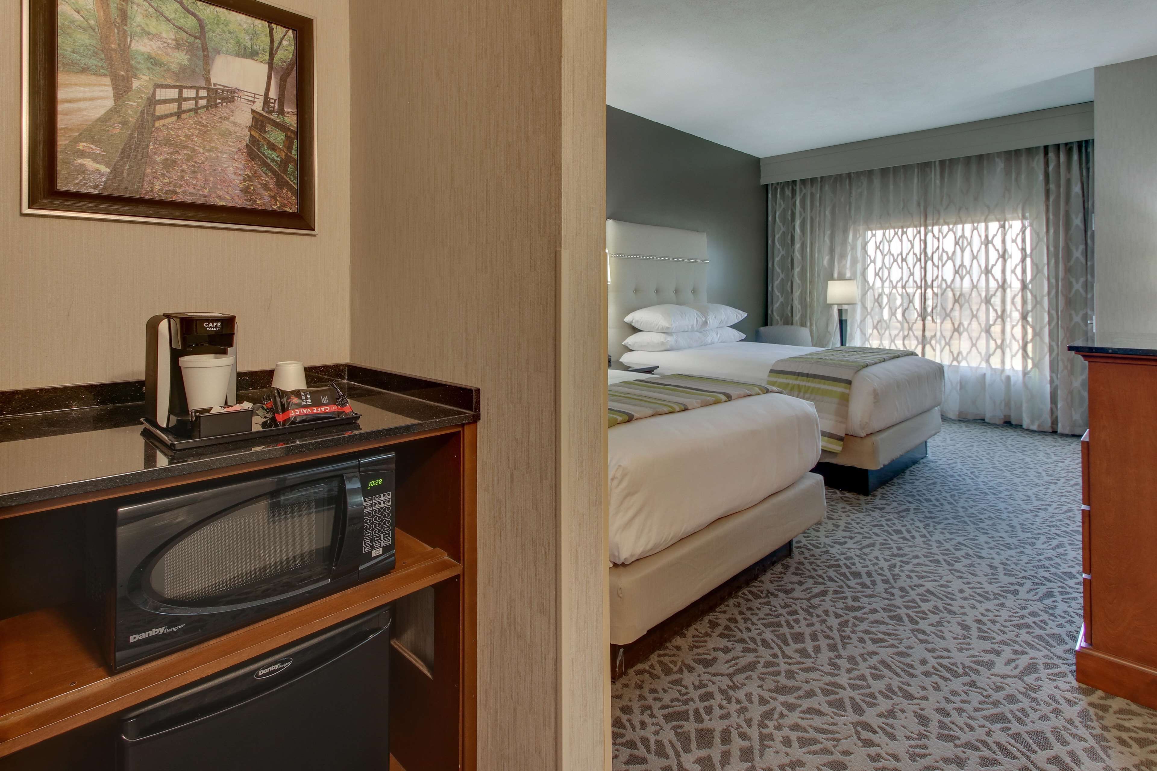 A hotel room with a bed, a microwave, a coffee maker, and a painting on the wall.