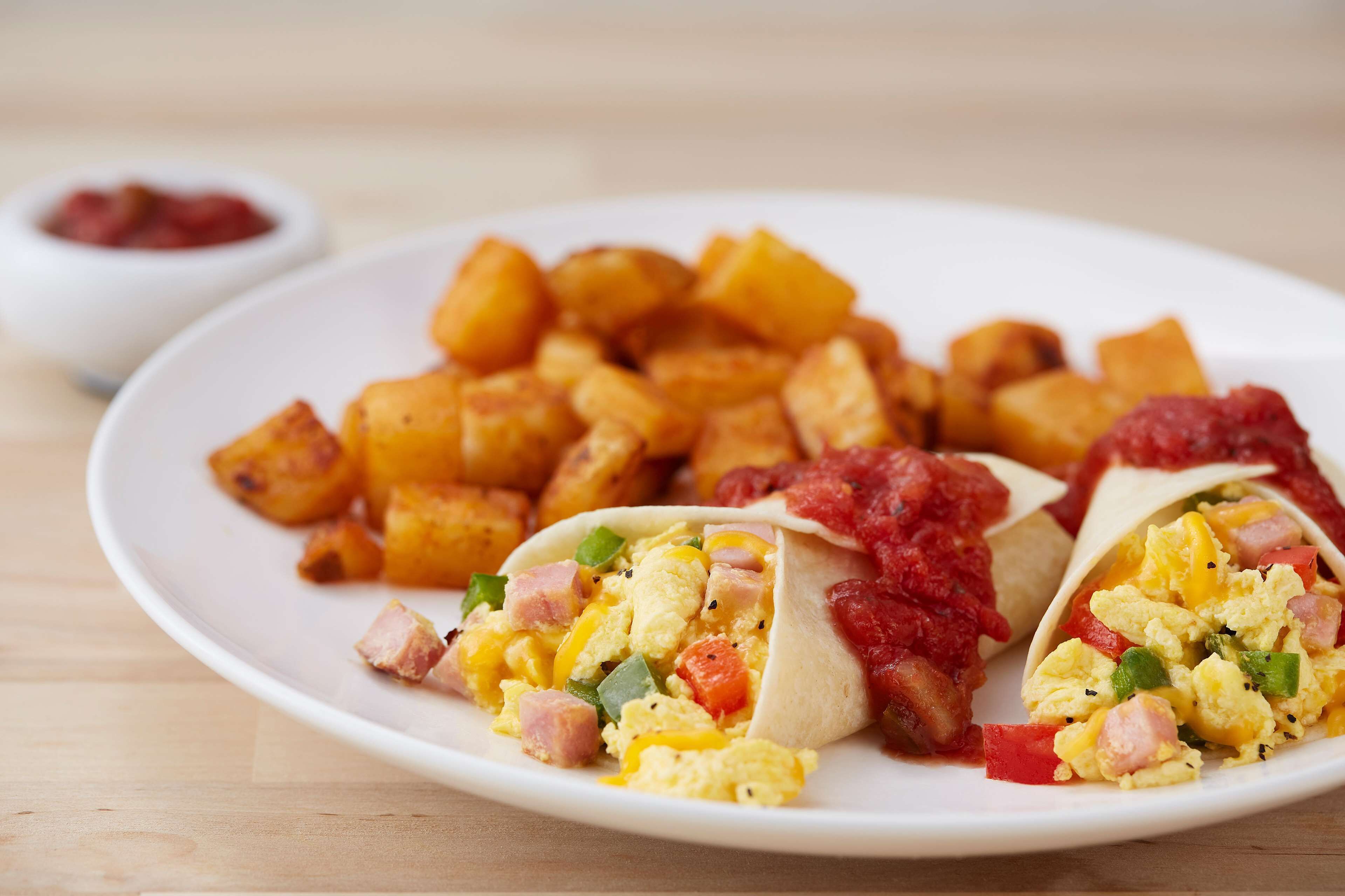 A plate with tacos, scrambled eggs, and roasted potatoes.