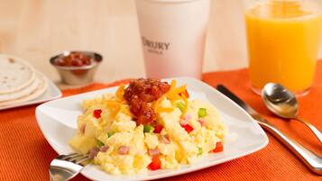 A breakfast plate with scrambled eggs, ham, and bell peppers, a coffee cup, and a glass of orange juice on an orange tablecloth.