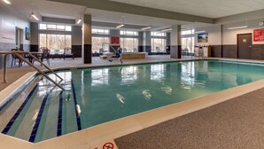Una piscina interior con agua azul cristalina, rodeada de sillas de descanso y una zona soleada con ventanas amplias.