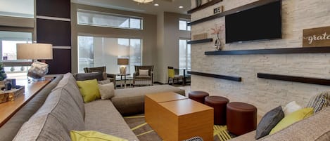 A modern living room with a sectional sofa, a wooden coffee table, and a flat-screen TV mounted on a brick wall.