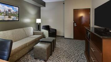 Una habitación de hotel con sofá, una silla, televisor, armario y puerta.