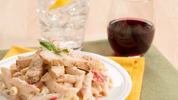 A plate of pasta with chicken and a glass of red wine.