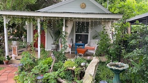 A covered porch with a garden, a blue chair, and a stone fountain. - Garden Cottage, Far From The Maddening Crowd but so close to the night life! (Dallas)