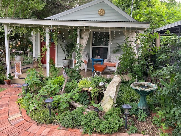 A covered porch with a garden, a blue chair, and a stone fountain.