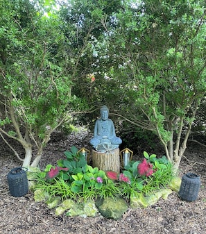 Una estatua de una figura sentada en un jardín con follaje y detalles decorativos.