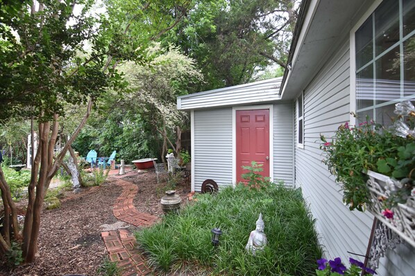 A garden with a red door, a white building, and various plants.