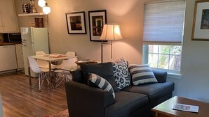A living room with a dark sofa, a patterned rug, a white couch, and a dining area with a table and chairs. - Garden Cottage, Far From The Maddening Crowd but so close to the night life! (Dallas)