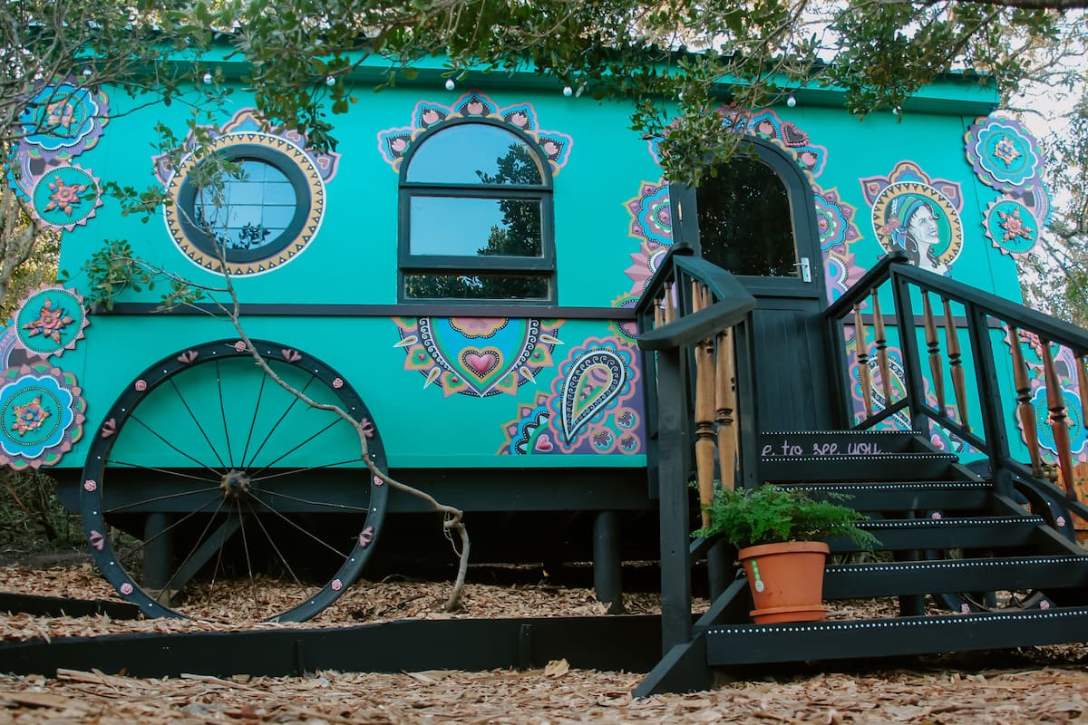 A turquoise house with intricate patterns, a large wheel, and a staircase leading to the entrance.
