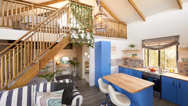 A modern kitchen with blue cabinets, a wooden island, and a staircase with a wooden railing. - Treedom Villas and Vardos (Wilderness)