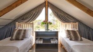A cozy attic bedroom with two beds, a shelf with shoes, and a window with curtains. - Treedom Villas and Vardos (Wilderness)