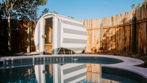 A swimming pool with a wooden fence and a cylindrical structure, possibly a sauna, in the background. - Treedom Villas and Vardos (Wilderness)