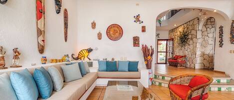 A spacious living area with a sofa, a coffee table, and a wicker chair. The room has a stone wall and a staircase leading to an upper level.