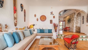 A spacious living area with a sofa, a coffee table, and a wicker chair. The room has a stone wall and a staircase leading to an upper level.