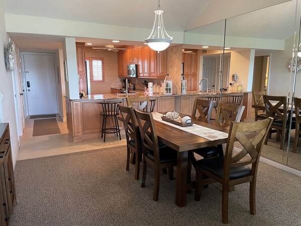 A spacious kitchen with wooden cabinets, a central island, and a dining area with a large table and chairs. - SIESTA DUNES 1-406 LUXURY CONDO WITH A GREAT VIEW! (Sarasota)