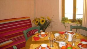 A dining area with a table set for two, a striped sofa, and a vase of sunflowers.