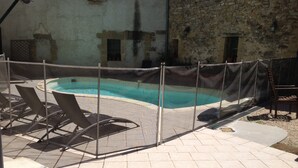 A pool area with a safety fence, lounge chairs, and a stone wall in the background.
